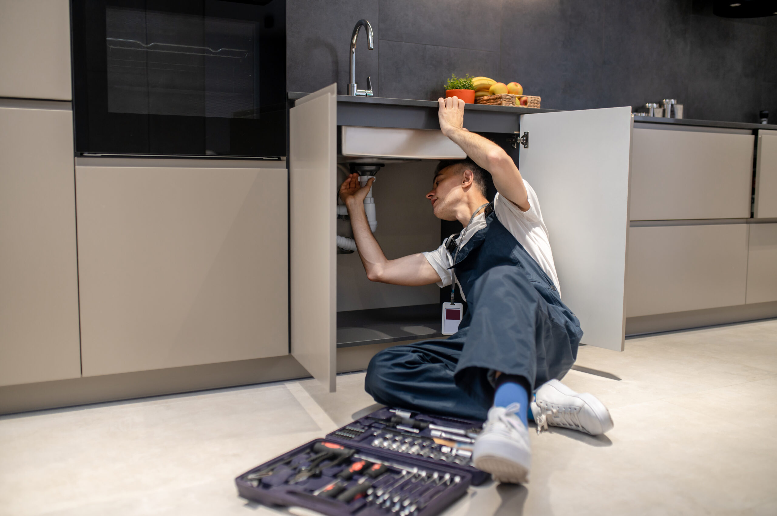 man reclining inspecting pipe under kitchen sink